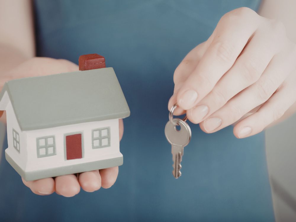 Pessoa segurando miniatura de casa e chave simbolizando mudança residencial e início de nova moradia, situação comum para quem busca aluguel em montes claros e está organizando a mudança para o novo imóvel.