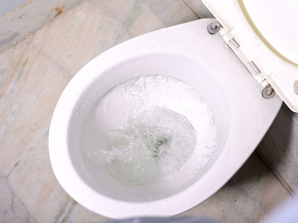 Vaso sanitário com água sendo acionada, ilustrando descarga em funcionamento e possível situação de vaso entupido com papel.